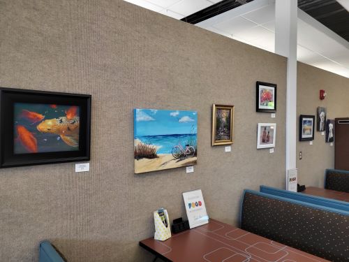 Eight framed paintings hung on a wall over several booths and tables.