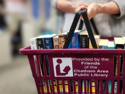 A woman carries a shopping basket brimming with colorful books.